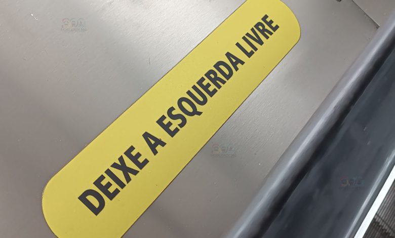 Adesivo amarelo com a inscrição 'Deixe a esquerda livre' colado ao lado de uma escada rolante.