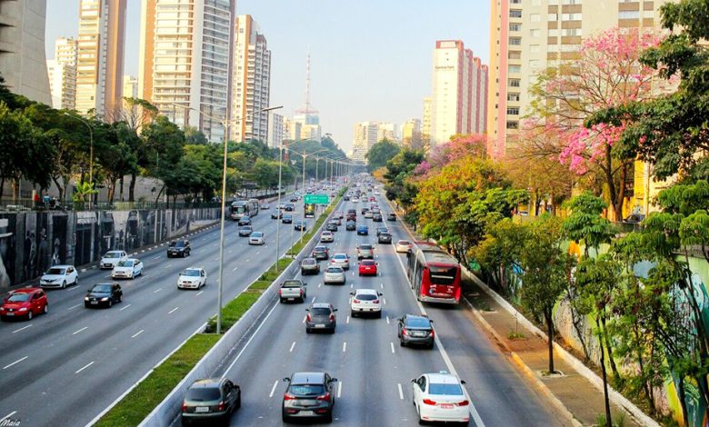 Avenida movimentada em São Paulo com carros e ônibus durante o dia, representando o custo de locomoção em São Paulo 2025.