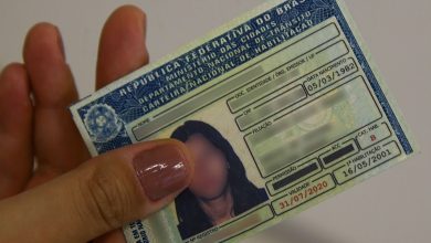 Carteira Nacional de Habilitação (CNH) brasileira sendo segurada por uma pessoa, com informações parcialmente borradas.