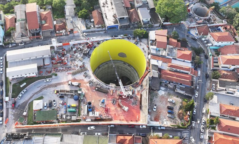 Poço de escavação da linha 6 do metrô de SP visto de cima, em área urbana com canteiro de obras ativo.