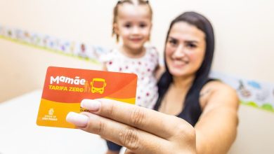 Mulher com filha segurando cartão Mamãe Tarifa Zero para transporte gratuito em São Paulo.