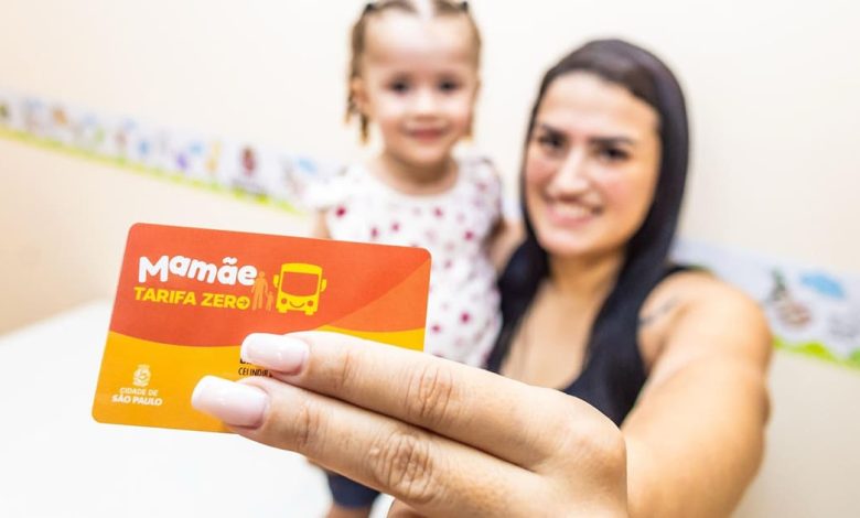 Mulher com filha segurando cartão Mamãe Tarifa Zero para transporte gratuito em São Paulo.