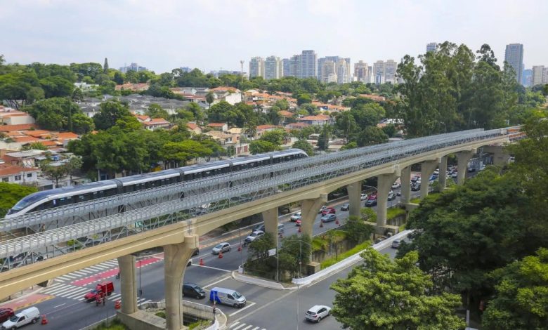 Primeiro trem da Linha 17-Ouro em teste na via elevada, com casas e edifícios ao fundo.