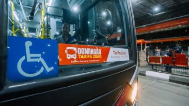 Ônibus com adesivo sobre tarifa zero em São Paulo estacionado em terminal urbano à noite.
