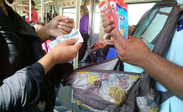 Vendedor ambulante no trem oferecendo produtos a passageiro, prática comum apesar da proibição do comércio ambulante nos trens.