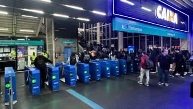 Passageiros em catracas de estação, exemplo de obras públicas no Brasil, com patrocínio de banco estatal em destaque.