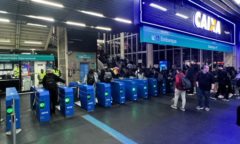 Passageiros em catracas de estação, exemplo de obras públicas no Brasil, com patrocínio de banco estatal em destaque.