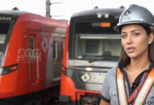 Mulher com capacete da CPTM e colete de segurança, com dois trens novos ao fundo, simboliza o futuro da CPTM.