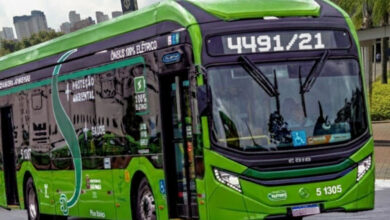 Ônibus verde da nova linha 4491/21 da SPTrans, elétrico, na rua, com prédios ao fundo.