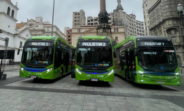 Três ônibus verdes das linhas Paulistar estacionados em praça de São Paulo com prédios históricos ao fundo.