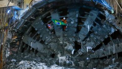 Operário com bandeira do Brasil na frente de tatuzão durante a escavação de túnel para a futura Linha 19-Celeste do Metrô.
