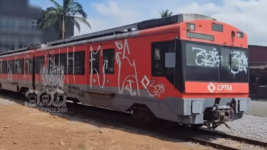 Foto do vagão pichado em Ribeirão Pires. O trem vermelho da CPTM está parado sobre trilhos e coberto por pichações brancas.