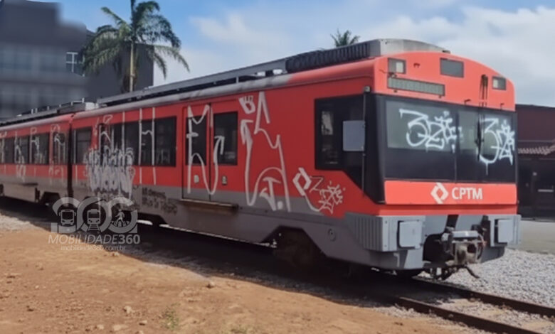 Foto do vagão pichado em Ribeirão Pires. O trem vermelho da CPTM está parado sobre trilhos e coberto por pichações brancas.