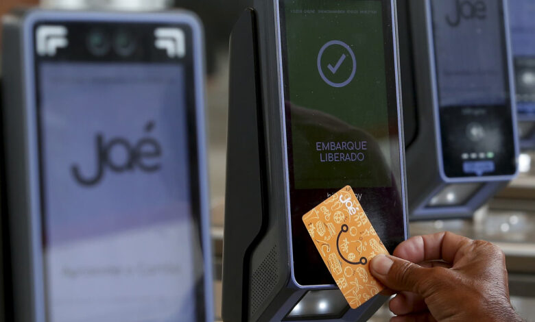 Mão de passageiro usa cartão Jaé em validador do sistema de Autopass bilhetagem, que exibe 