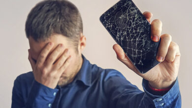 Homem frustrado segurando celular com tela quebrada, simbolizando a necessidade de descarte de lixo eletrônico.