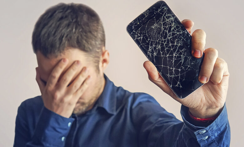 Homem frustrado segurando celular com tela quebrada, simbolizando a necessidade de descarte de lixo eletrônico.