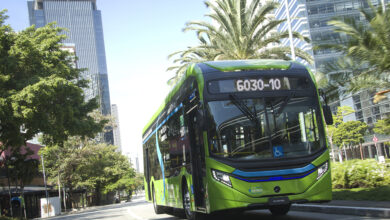 Ônibus elétrico Mercedes-Benz eO500 U verde circulando em avenida urbana de São Paulo, com prédios ao fundo.