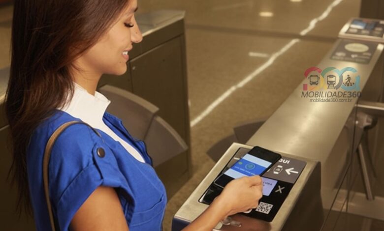 Passageira utiliza o celular para fazer o pagamento por aproximação no MetrôRio, encostando o aparelho no validador da catraca.