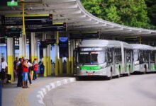 Passageiros esperam ônibus articulado em terminal de SP, onde vozes infantis terminais de ônibus transmitirão avisos.